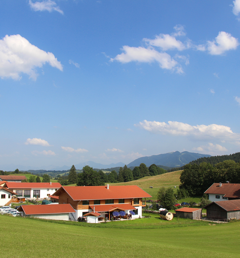 Landschaft mit ländlichen Gebäuden und Bergen unter blauem Himmel.