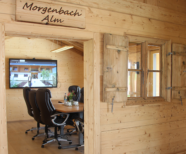 Moderner Besprechungsraum in der Morgenbach Alm mit Holzverkleidung und komfortablen Bürostühlen. Im Hintergrund ist ein Bildschirm zu sehen.