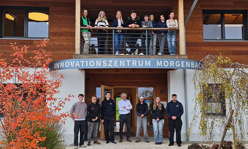 Gruppe von Personen steht vor einem Gebäude mit der Aufschrift „Innovationszentrum Morgenbach“, umgeben von herbstlichen Bäumen.