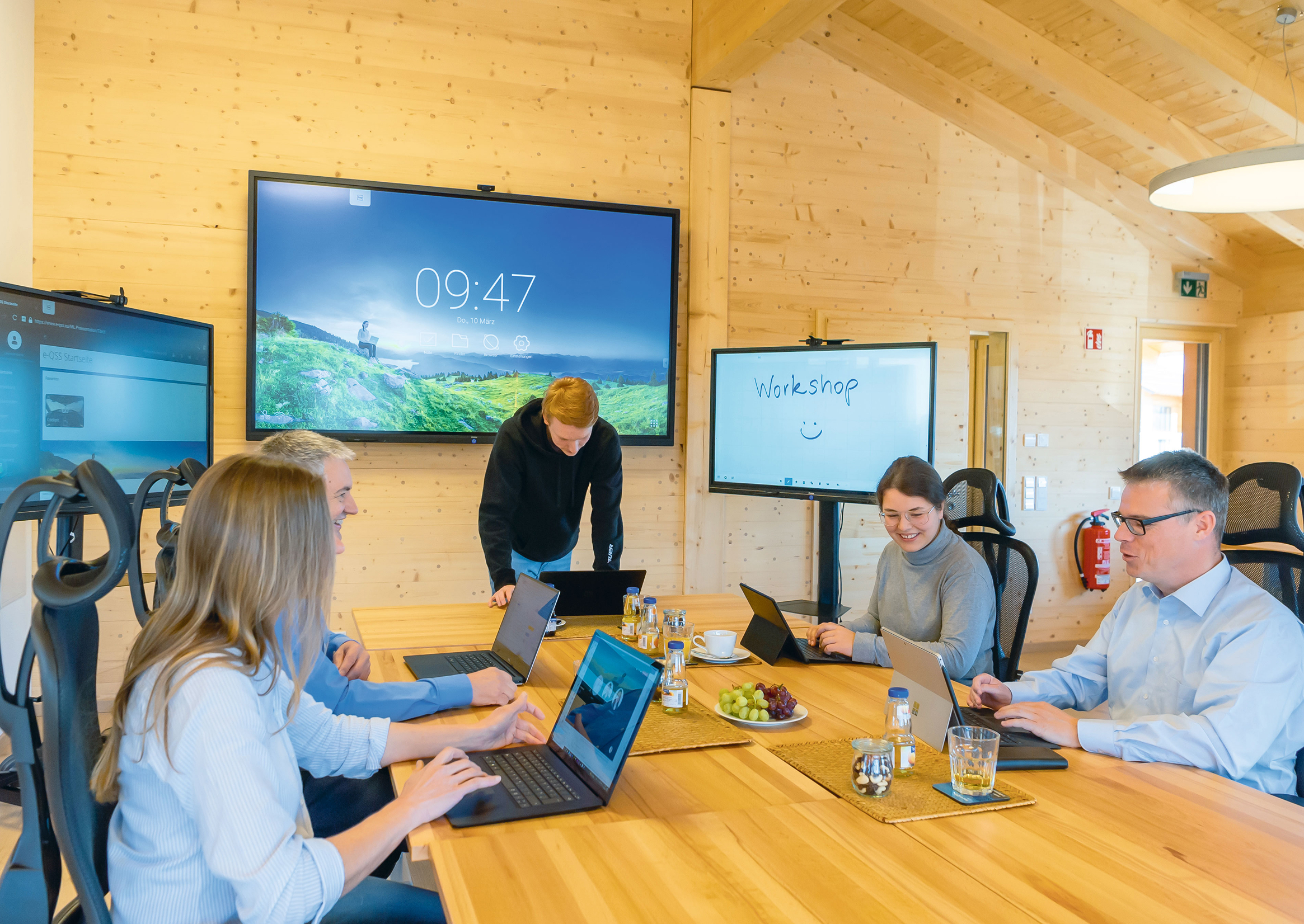 Team arbeitet in einem modernen Konferenzraum an Laptops während eines Workshops mit Präsentationsbildschirmen.