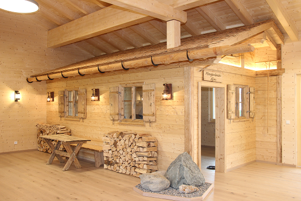 Gemütlicher Innenraum mit der integrierten Morgenbach Almhütte mit Holzverkleidung, Sitzbank, Holzstapel und dekorativen Steinen.