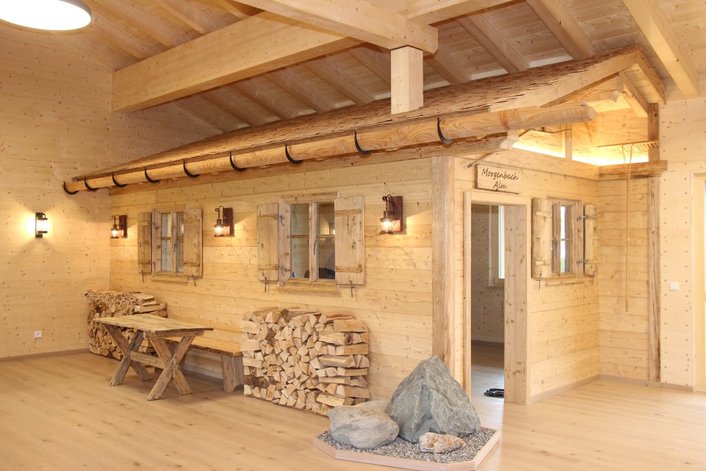 Gemütlicher Innenraum mit der integrierten Morgenbach Almhütte mit Holzverkleidung, Sitzbank, Holzstapel und dekorativen Steinen.